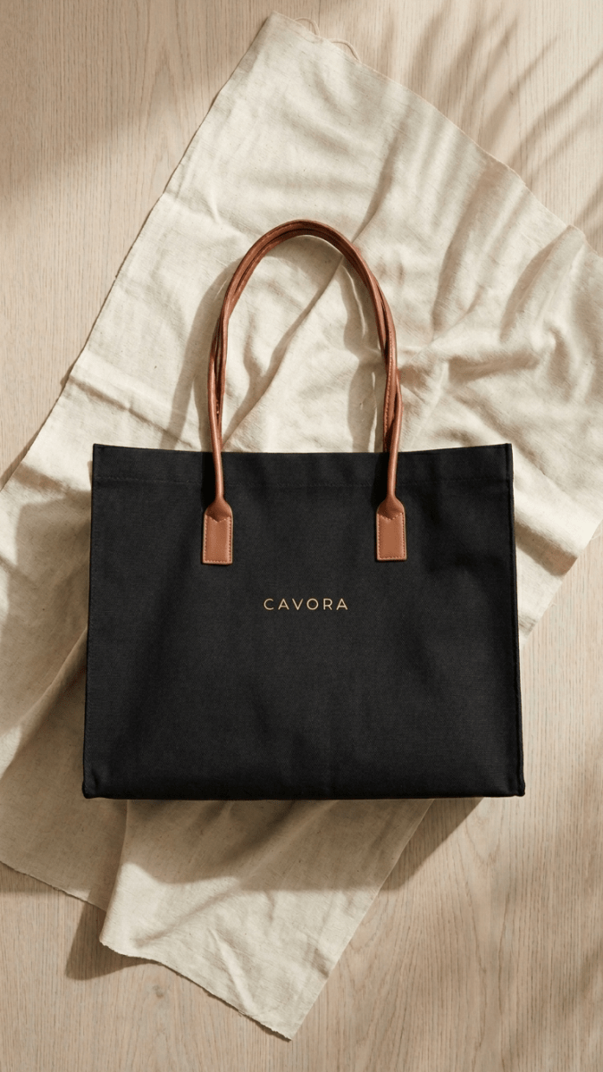 Black tote bag with brown handles on a light fabric background